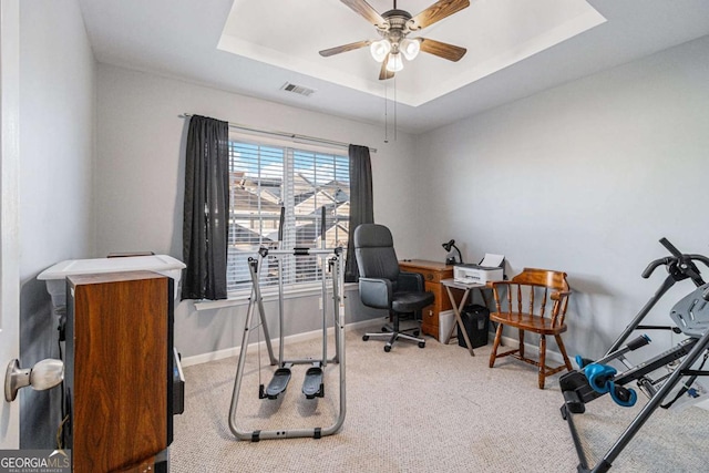 carpeted office space featuring ceiling fan and a raised ceiling