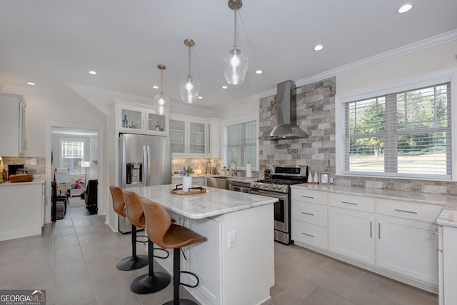 kitchen featuring white cabinets, appliances with stainless steel finishes, a center island, and wall chimney exhaust hood