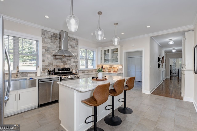 kitchen featuring white cabinetry, stainless steel appliances, wall chimney range hood, decorative light fixtures, and a kitchen island