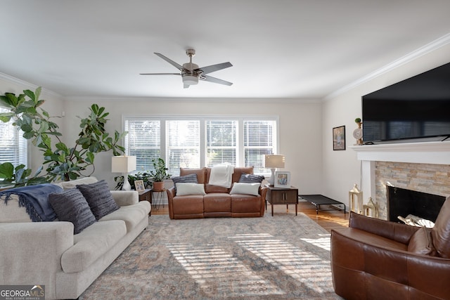 living room featuring hardwood / wood-style floors, a stone fireplace, ceiling fan, and ornamental molding