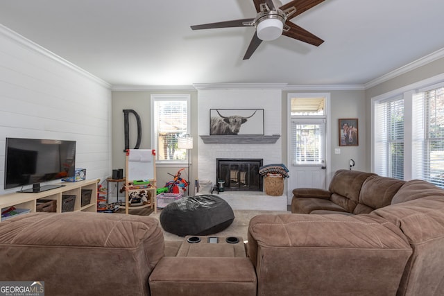 living room featuring ceiling fan, plenty of natural light, ornamental molding, and a brick fireplace