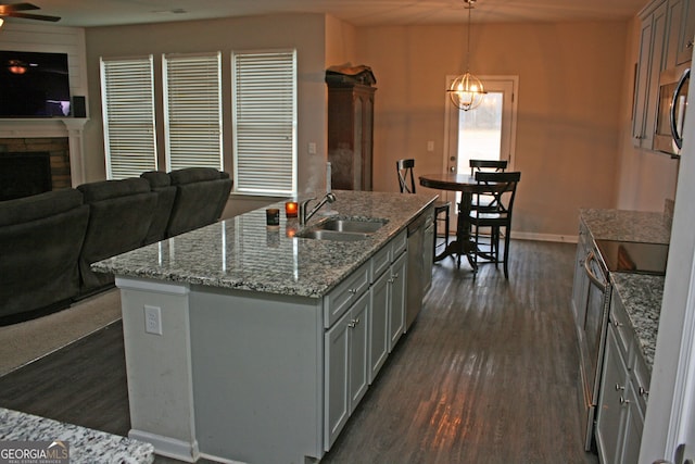 kitchen with a stone fireplace, a kitchen island with sink, hanging light fixtures, dark hardwood / wood-style floors, and sink