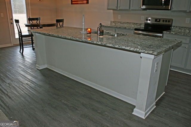 kitchen with stainless steel range with electric stovetop, dark wood-type flooring, sink, and an island with sink