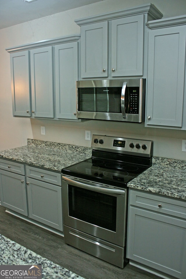 kitchen with gray cabinetry, stainless steel appliances, light stone counters, and dark hardwood / wood-style floors