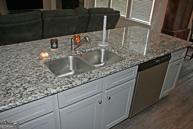 kitchen featuring light stone counters, dark wood-type flooring, stainless steel dishwasher, and sink