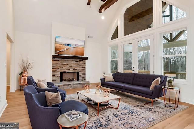 living room with beamed ceiling, light wood-type flooring, high vaulted ceiling, and a stone fireplace