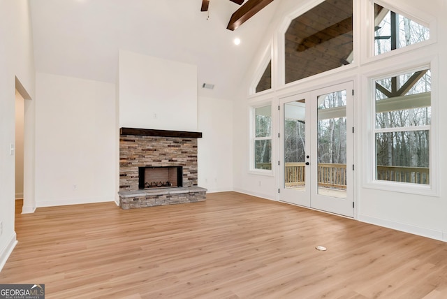 unfurnished living room featuring french doors, light wood-type flooring, beam ceiling, high vaulted ceiling, and a stone fireplace