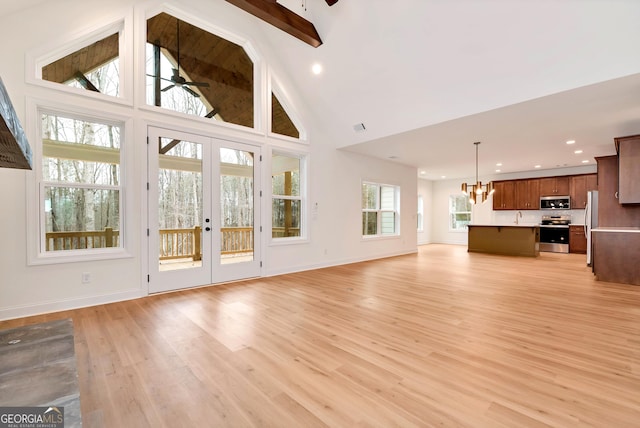 unfurnished living room featuring french doors, light wood-type flooring, ceiling fan with notable chandelier, beam ceiling, and high vaulted ceiling