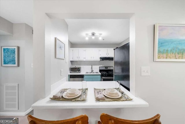 kitchen with white cabinetry, stainless steel appliances, tasteful backsplash, range hood, and a kitchen bar