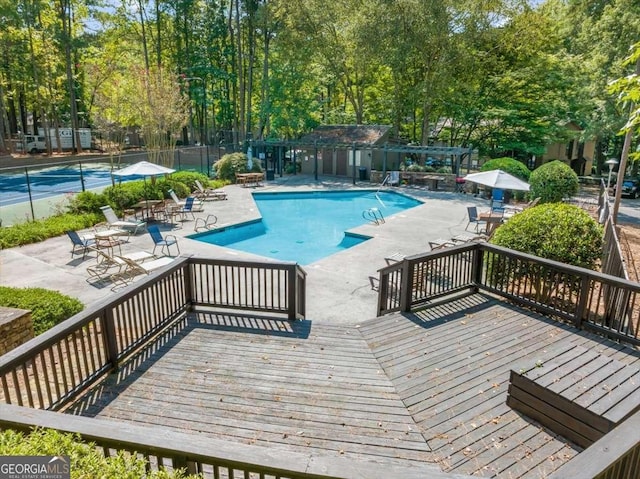 view of swimming pool featuring a deck and tennis court