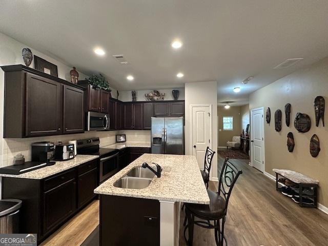 kitchen featuring a kitchen island with sink, sink, light hardwood / wood-style floors, light stone counters, and stainless steel appliances