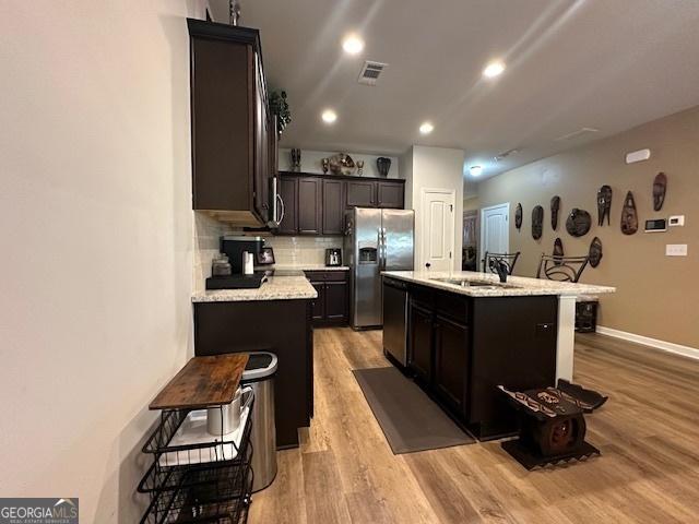 kitchen featuring decorative backsplash, light wood-type flooring, stainless steel appliances, a kitchen island with sink, and sink