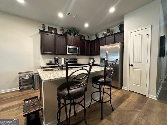 kitchen featuring light stone counters, dark brown cabinetry, stainless steel appliances, sink, and a center island with sink