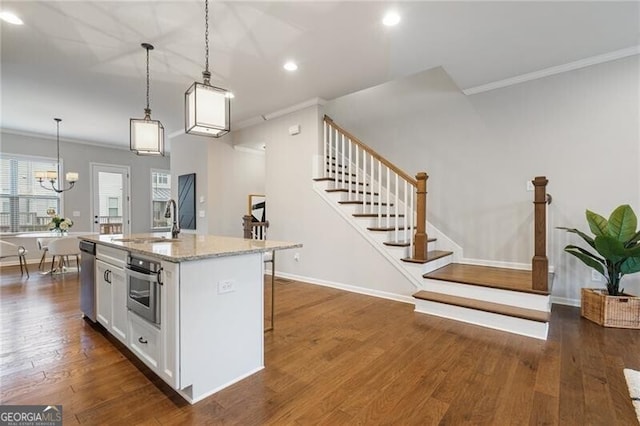 kitchen featuring appliances with stainless steel finishes, sink, decorative light fixtures, white cabinets, and an island with sink