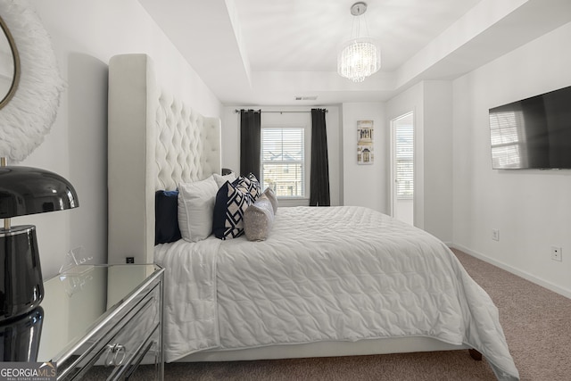 carpeted bedroom with a raised ceiling and an inviting chandelier