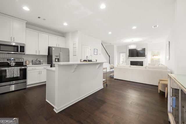 kitchen featuring decorative backsplash, appliances with stainless steel finishes, a kitchen island, white cabinetry, and a breakfast bar area