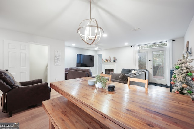 dining space with french doors, light wood-type flooring, and a notable chandelier