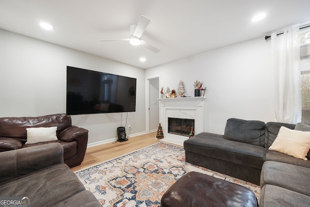 living room featuring a premium fireplace, light hardwood / wood-style flooring, and ceiling fan