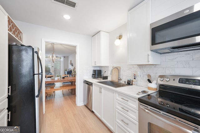 kitchen featuring white cabinetry, sink, a chandelier, light hardwood / wood-style floors, and appliances with stainless steel finishes