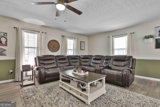 living room with a textured ceiling, ceiling fan, wood finished floors, visible vents, and baseboards