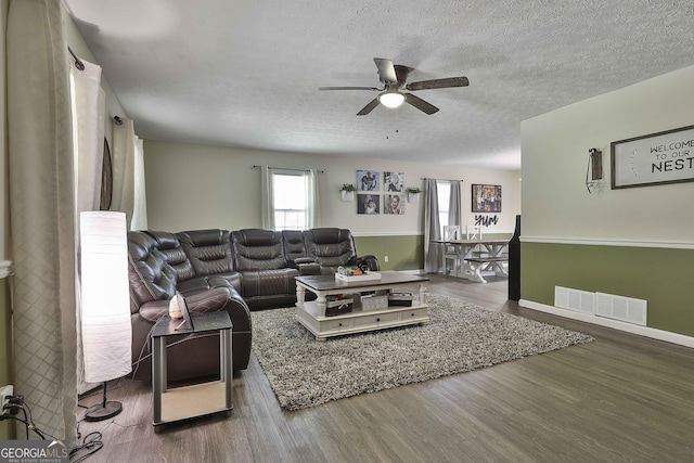 living area with ceiling fan, a textured ceiling, wood finished floors, and visible vents