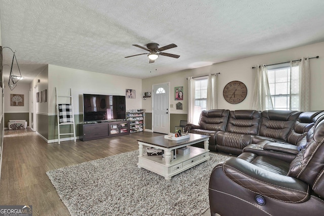 living area with ceiling fan, a textured ceiling, and wood finished floors