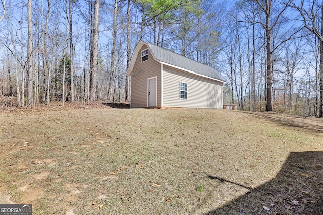 view of home's exterior featuring an outbuilding, a lawn, roof with shingles, and a gambrel roof