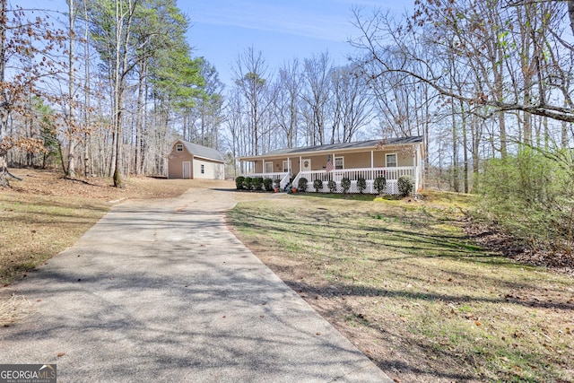 view of front of house featuring aphalt driveway, a front lawn, a porch, and an outbuilding