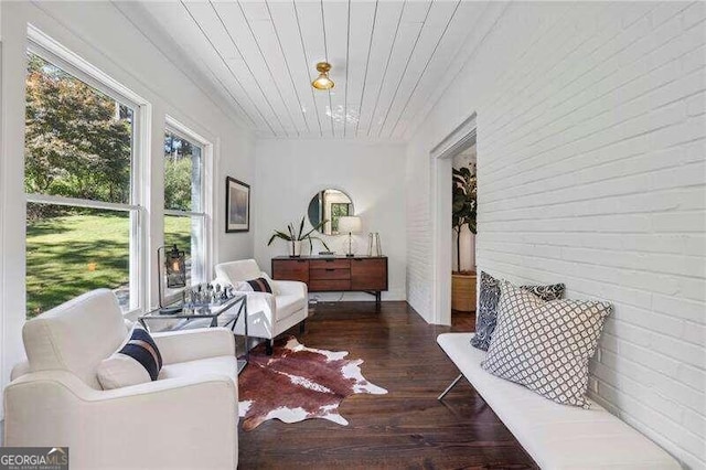 sitting room with dark hardwood / wood-style floors, wooden ceiling, and brick wall