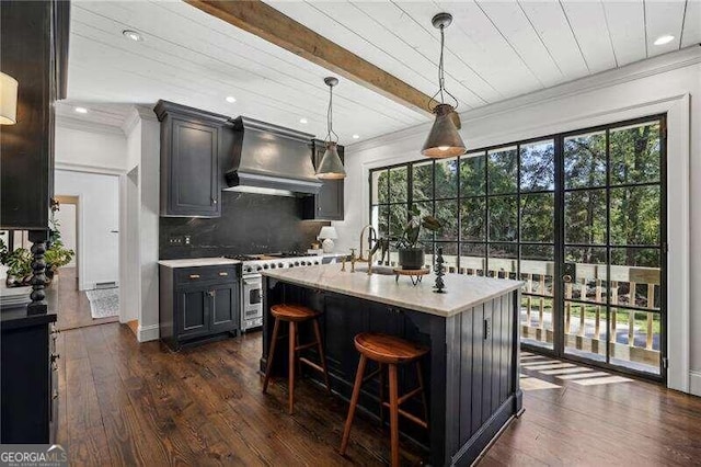 kitchen featuring wall chimney exhaust hood, hanging light fixtures, dark hardwood / wood-style floors, an island with sink, and high end range