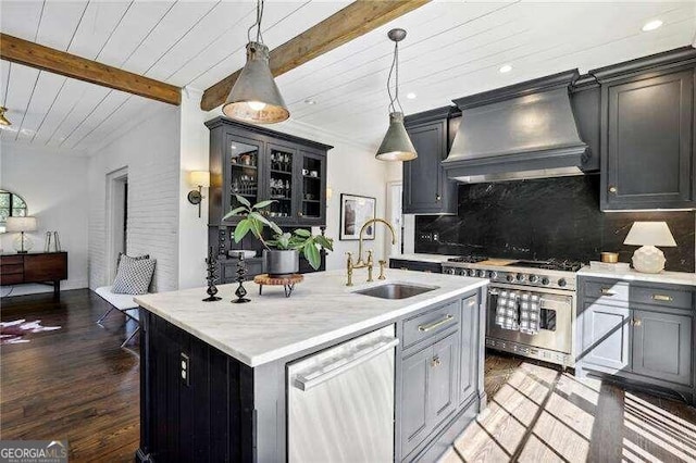 kitchen with custom exhaust hood, a kitchen island with sink, hanging light fixtures, sink, and appliances with stainless steel finishes