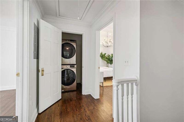 laundry area with dark wood-type flooring, crown molding, stacked washer and clothes dryer, a notable chandelier, and electric panel