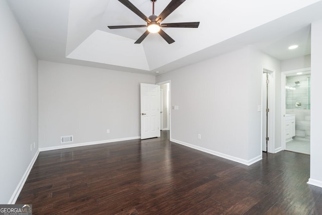 empty room with dark hardwood / wood-style flooring, a tray ceiling, and ceiling fan