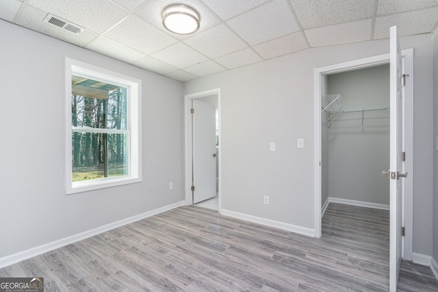 unfurnished bedroom featuring a spacious closet, a closet, a drop ceiling, and light wood-type flooring