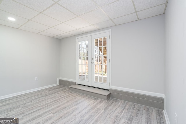 unfurnished room featuring french doors, light wood-type flooring, and a drop ceiling