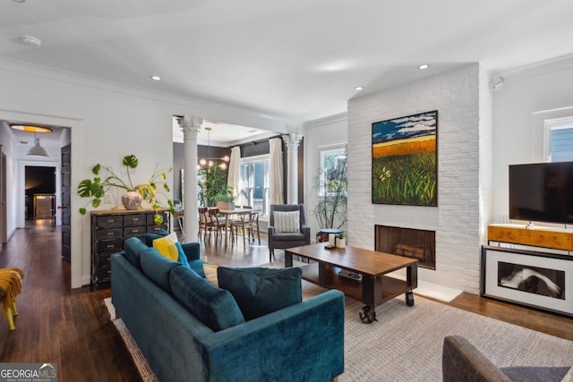 living room featuring hardwood / wood-style flooring, ornate columns, ornamental molding, and a brick fireplace