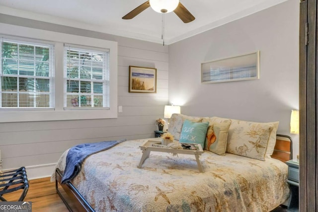 bedroom featuring ceiling fan, crown molding, wood-type flooring, and wooden walls