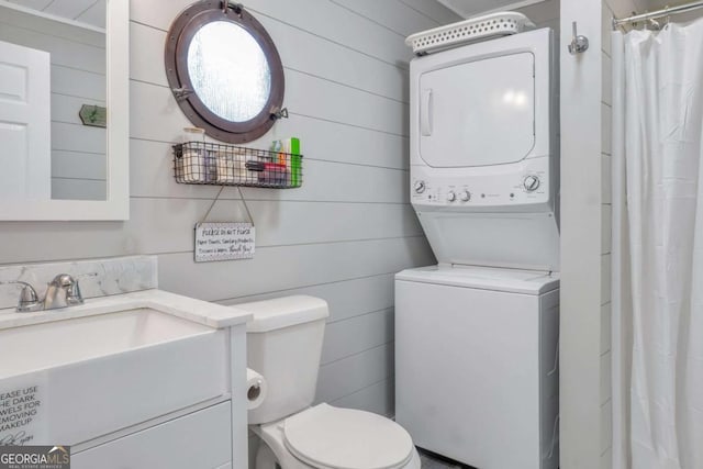 bathroom featuring wooden walls, stacked washer / drying machine, toilet, and vanity