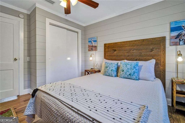 bedroom featuring dark wood-type flooring, crown molding, wooden walls, ceiling fan, and a closet