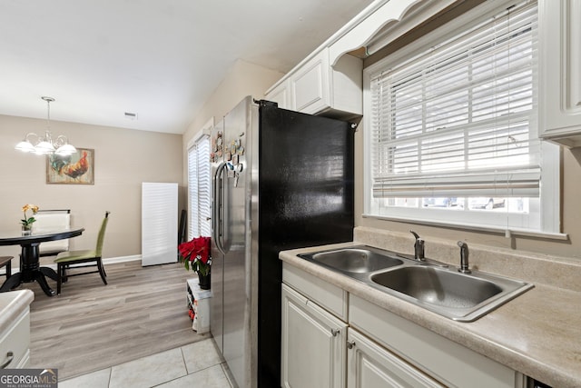 kitchen with stainless steel refrigerator, white cabinetry, sink, hanging light fixtures, and a notable chandelier