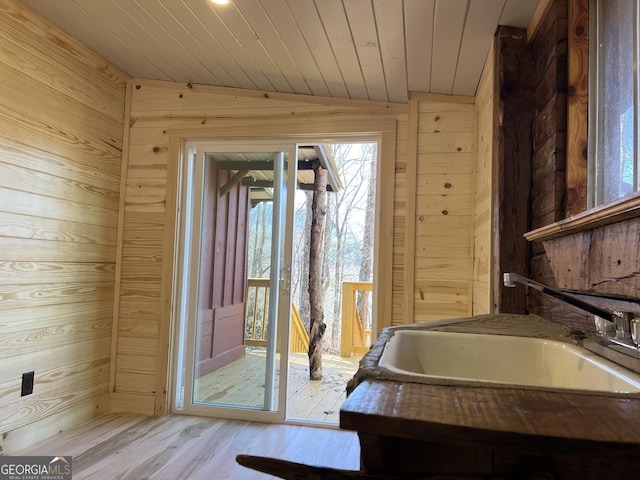 doorway featuring wooden walls, sink, wood ceiling, and light hardwood / wood-style floors