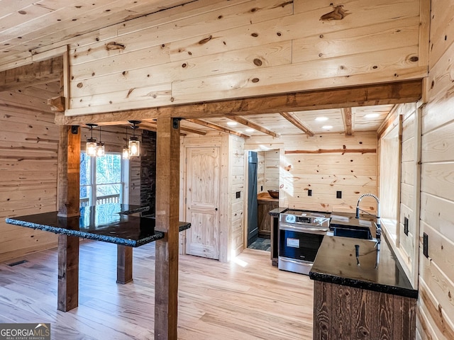 kitchen featuring wood walls, sink, light hardwood / wood-style flooring, stainless steel range, and decorative light fixtures