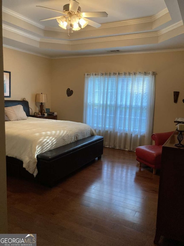 bedroom with dark wood-type flooring, a raised ceiling, ceiling fan, and ornamental molding