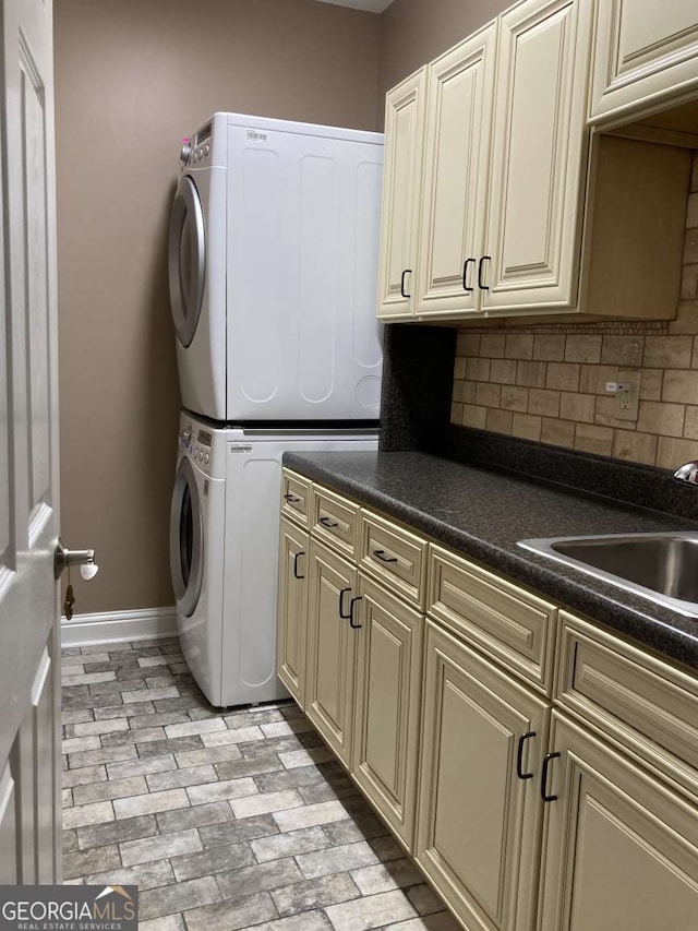 laundry area featuring cabinets, stacked washer / dryer, and sink