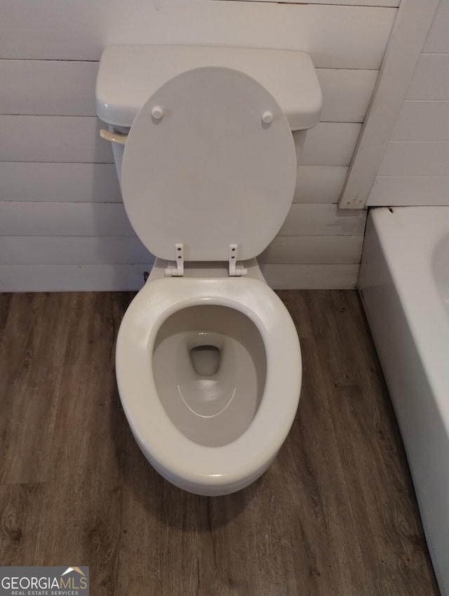 interior details featuring wood walls, toilet, wood-type flooring, and a bath