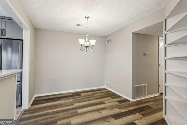 unfurnished dining area featuring a textured ceiling, dark wood-type flooring, and a notable chandelier