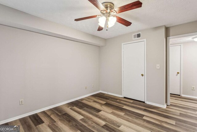 unfurnished bedroom with ceiling fan, dark hardwood / wood-style flooring, and a textured ceiling