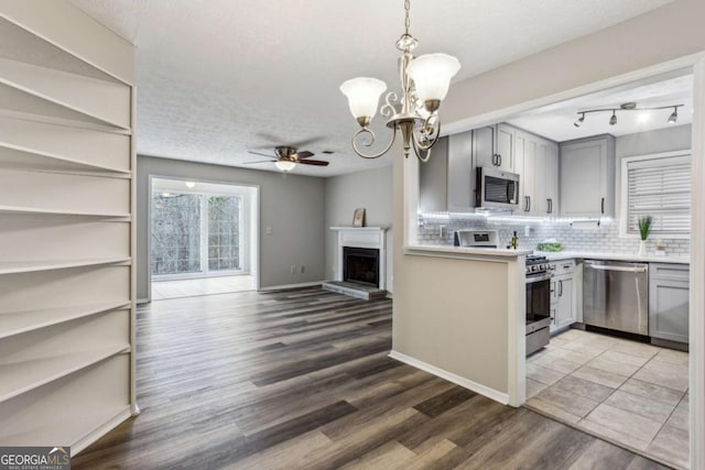 kitchen with pendant lighting, ceiling fan with notable chandelier, dark hardwood / wood-style floors, gray cabinets, and appliances with stainless steel finishes