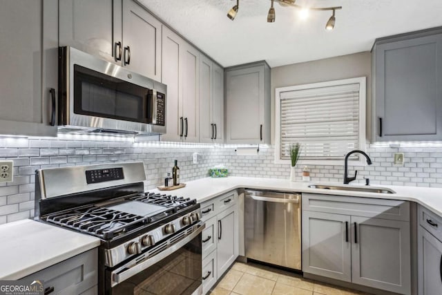 kitchen featuring appliances with stainless steel finishes, backsplash, gray cabinetry, sink, and light tile patterned floors