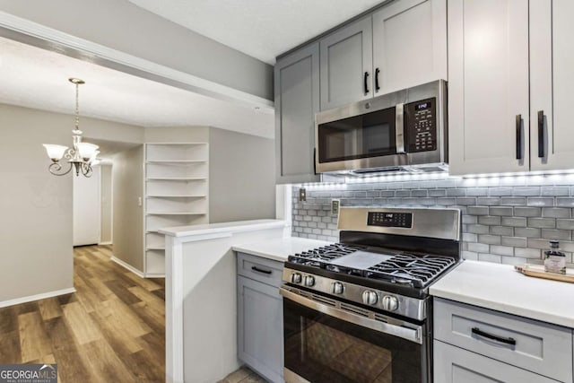 kitchen with stainless steel appliances, an inviting chandelier, pendant lighting, gray cabinets, and decorative backsplash